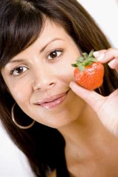 Portrait of a young woman holding a strawberry and smiling