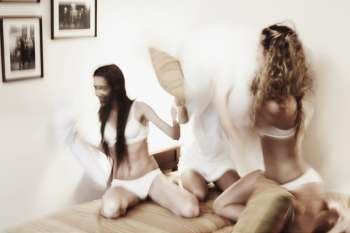 Three young women having a pillow fight on the bed