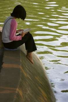 Side profile of a girl reading a book at the riverside, Hanoi, Vietnam