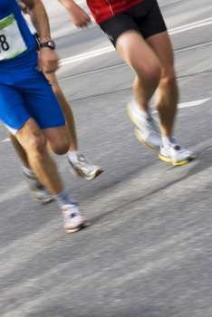Low section view of three male athletes running on a running track