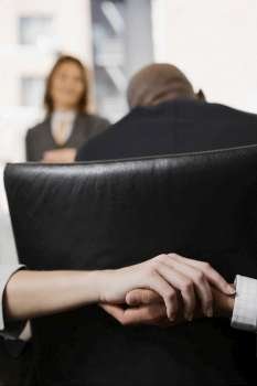 Close-up of a man´s hand holding a woman´s hand behind a chair in an office
