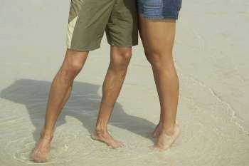 Low section view of a young man and a teenage girl standing on the beach