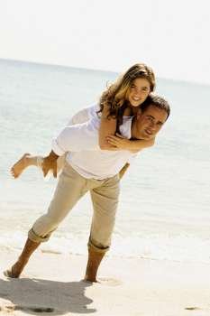 Portrait of a young woman riding piggyback on a mid adult man on the beach