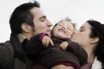 Close-up of a couple kissing their daughter