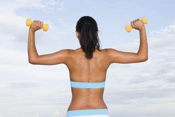 Rear view of a young woman lifting dumbbells