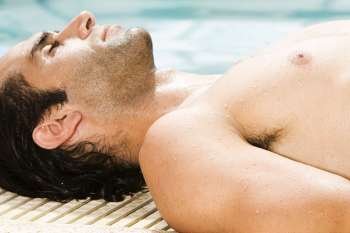 Side profile of a mid adult man lying at the edge of a pool