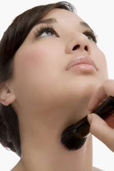 Close-up of a young woman holding a make-up brush and applying make-up