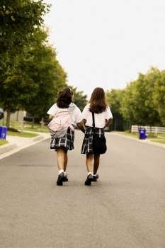 Rear view of two schoolgirls walking on the road