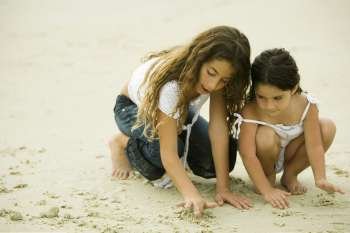 Two sisters playing with sand on the beach