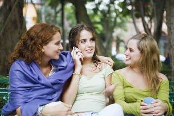 Close-up of a young woman talking on a mobile phone and sitting with her two friends
