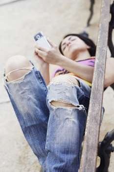 Mid adult woman lying on a bench and using a mobile phone 