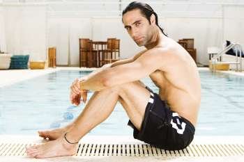 Side profile of a mid adult man sitting at the edge of a swimming pool