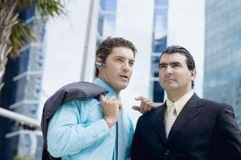Businessman using a bluetooth device and another businessman standing in front of him