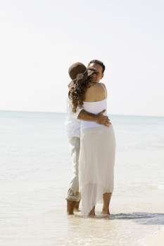 Rear view of a young woman and a mid adult man embracing each other on the beach