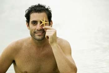 Portrait of a mid adult man holding a starfish in front of his eye
