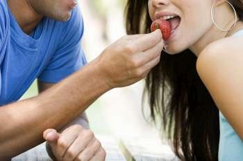 Close-up of a mid adult man feeding a young woman a strawberry