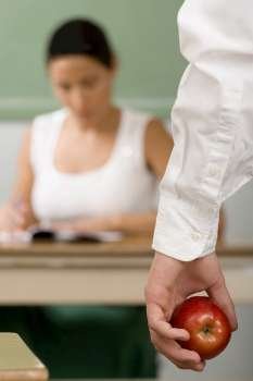 Close-up of a person´s hand holding an apple with a female teacher sitting in the background