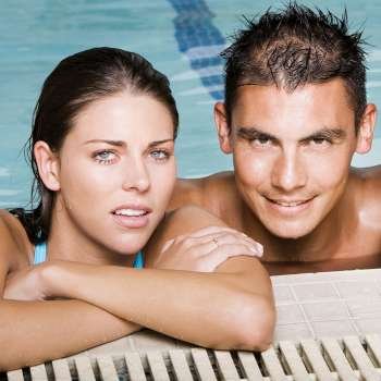 Portrait of a young couple leaning at the edge of a swimming pool