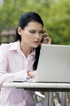 Close-up of a businesswoman talking on a mobile phone while using a laptop