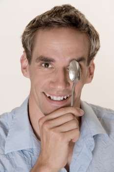 Portrait of a young man covering his eye with a spoon