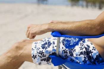 Mid section view of a man sitting in an armchair on the beach