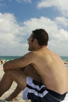 Side profile of a mid adult man sitting on the beach