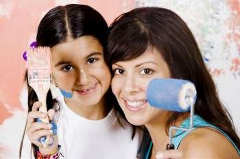 Portrait of a young woman holding a paint roller with her daughter holding a paintbrush