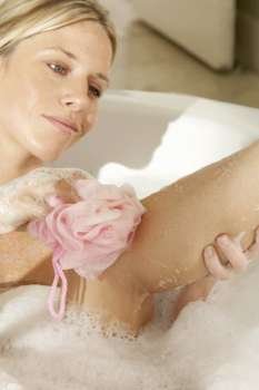 Young woman scrubbing her leg with a bath sponge in a bathtub