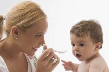 Mid adult woman feeding her son with a spoon and smiling