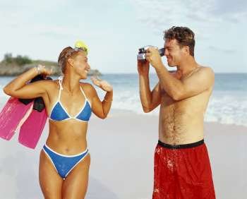 Close-up of a young man taking a photograph of a young woman holding flippers, Bermuda