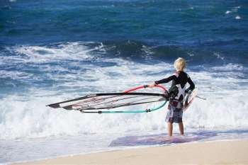 Rear view of a person holding a windsurfing board on the beach, Hookipa Beach Park, Maui, Hawaii Islands, USA