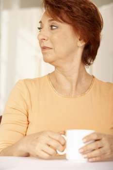 Close-up of a senior woman holding a cup of coffee and looking sideways
