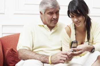 Close-up of a mature man sitting with his daughter on a couch and looking at a mobile phone