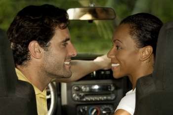 Young woman and a mid adult man sitting in a car looking at each other