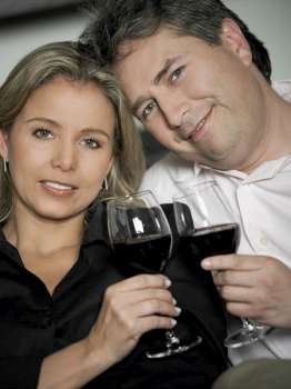 Portrait of a mid adult woman and a mature man toasting glasses of red wine and smiling