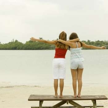 Rear view of girl and a teenage girl standing with their arms around each other on a picnic table
