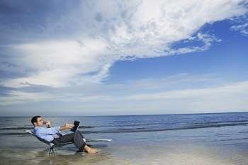 Side profile of a young man sitting on the beach with a laptop 