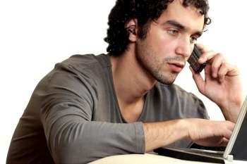 Close-up of a young man talking on a mobile phone using a laptop