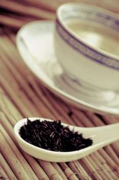 Tea leaves in a tea spoon with a tea cup
