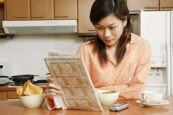 Close-up of a young woman reading a newspaper at a kitchen counter