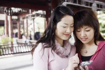 Close-up of a young woman with her friend holding a mobile phone