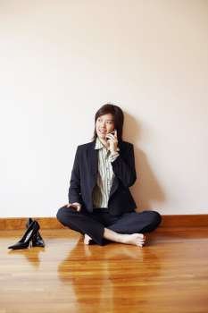 Businesswoman sitting on the hardwood floor and talking on a mobile phone