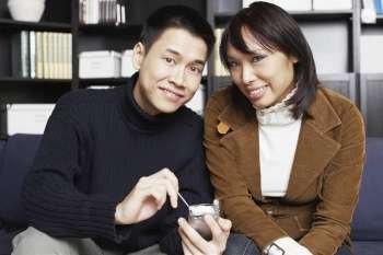 Portrait of a young man sitting with a young woman on a couch holding a mobile phone