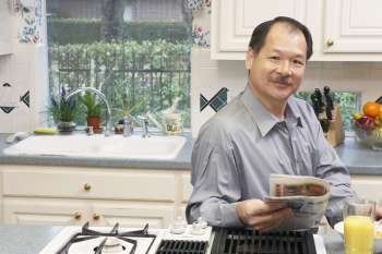 Portrait of a senior man holding a newspaper in the kitchen