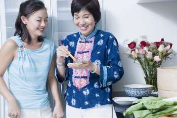 Senior woman preparing food with her granddaughter standing behind her and smiling