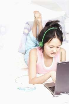 High angle view of a girl using a laptop listening to music on an MP3 player