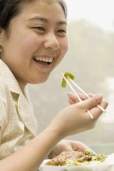Close-up of a female office worker having lunch with chopsticks and smiling