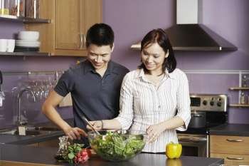 Young man standing looking at a young woman preparing food
