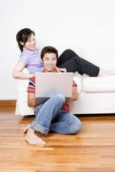 Young woman sitting on a couch with a mid adult man using a laptop