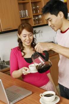Close-up of a mid adult man serving tea to a young woman at a kitchen counter